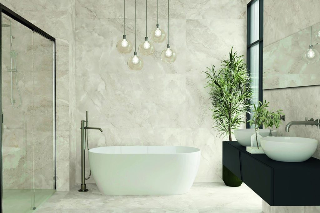 Azulejos Benadresa Aura Ivory bathroom with patterned pale surfaces, a white bath and dark fittings.